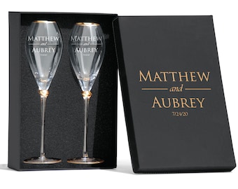 May include: Two champagne flutes with gold rims in a black box. The flutes are engraved with the names "Matthew and Aubrey" and the date "7/24/20".