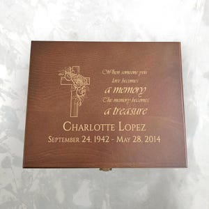May include: A brown wooden box with engraved text and a cross design. The text includes the name "CHARLOTTE LOPEZ" and dates "SEPTEMBER 24, 1942 - MAY 28, 2014", along with the quote "When someone you love becomes a memory, the memory becomes a treasure."