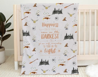 May include: A soft, gray baby blanket with a Harry Potter theme. The blanket features a repeating pattern of Hogwarts castle, glasses, wands, owls, and the number 9 3/4. The text on the blanket reads "Happiness can be found even in the darkest of times if one only remembers to turn on the light."