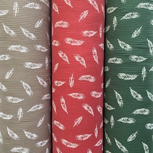 May include: Three rolls of fabric with a white feather pattern on a green, red, and beige background.