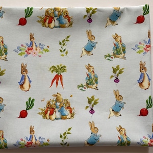 Pu&ograve; includere: Tessuto blu con un motivo ripetuto di personaggi di Peter Rabbit, tra cui Peter Rabbit, Benjamin Bunny e altri conigli. Il tessuto presenta uno sfondo blu chiaro con contorni bianchi attorno ai personaggi. Il tessuto presenta anche carote, ravanelli e altre verdure.