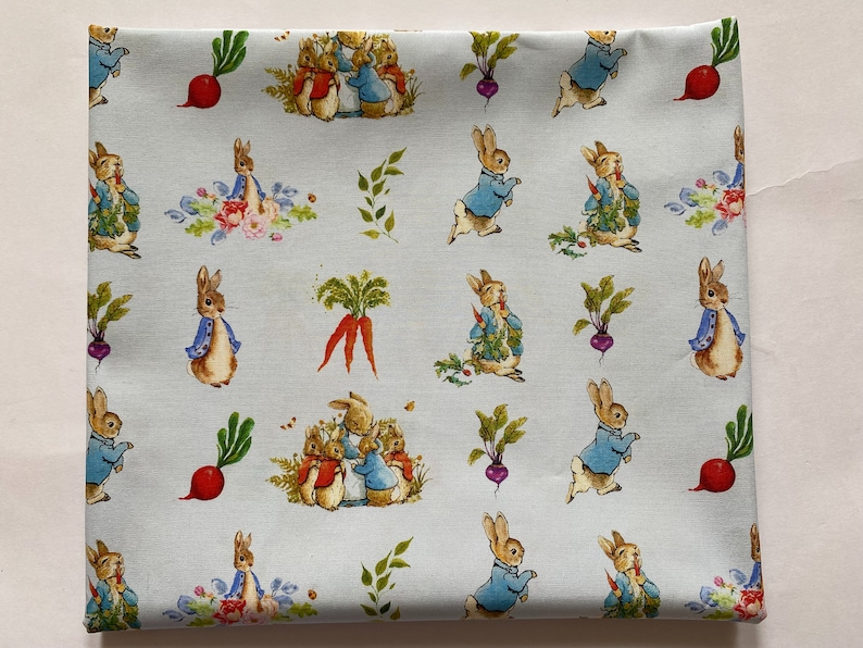 Pu&ograve; includere: Tessuto blu con un motivo ripetuto di personaggi di Peter Rabbit, tra cui Peter Rabbit, Benjamin Bunny e altri conigli. Il tessuto presenta uno sfondo blu chiaro con contorni bianchi attorno ai personaggi. Il tessuto presenta anche carote, ravanelli e altre verdure.