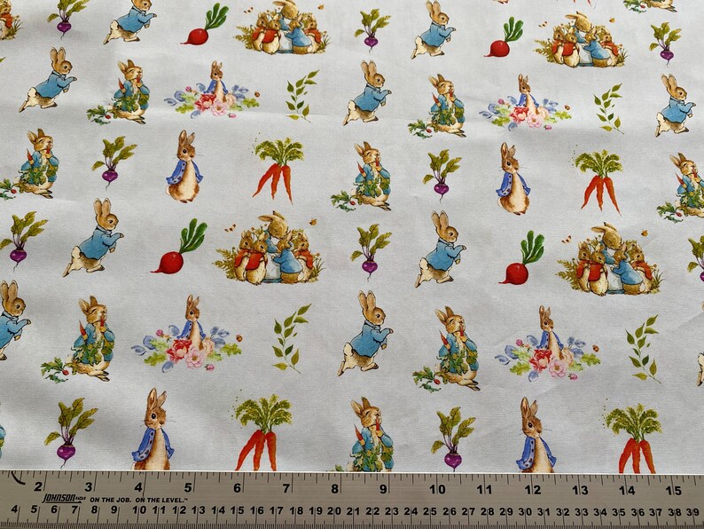 Pu&ograve; includere: Un tessuto bianco con un motivo ripetuto di personaggi di Peter Rabbit. I personaggi sono in varie pose, tra cui in piedi, seduti e che tengono carote. Il tessuto presenta anche foglie verdi, ravanelli rossi e rape viola.