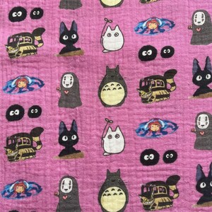 Puede incluir: Tela rosa con un patr&oacute;n repetido de personajes animados, incluyendo una criatura gris grande, un gato negro, un gato blanco, un veh&iacute;culo tipo autob&uacute;s y una ni&ntilde;a en una burbuja azul. Una regla est&aacute; en la parte inferior.