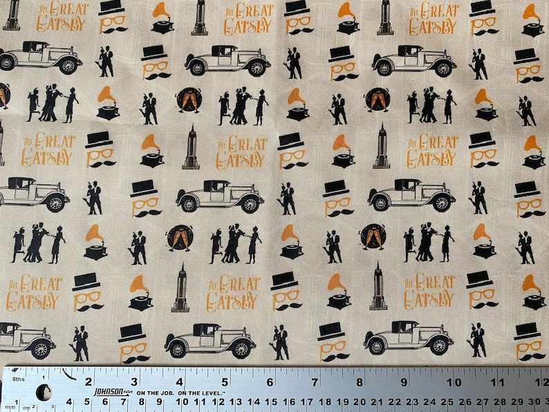 May include: A beige fabric with a repeating pattern of black silhouettes of people dancing, cars, and buildings. The text "The Great Gatsby" is repeated throughout the pattern in orange lettering.