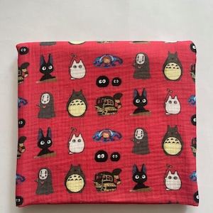 Puede incluir: Tela roja plegada con un estampado repetido de personajes de dibujos animados. El dise&ntilde;o incluye varias criaturas en negro, blanco y gris, con algunos toques de azul. La tela est&aacute; doblada, lo que sugiere que podr&iacute;a ser una bufanda o un accesorio similar.