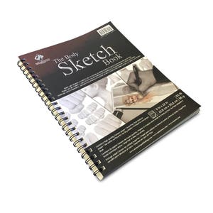 May include: A black and white spiral bound sketchbook with the text "The Body Sketch Book" on the cover. The cover also features a drawing of a hand holding a pencil and a series of anatomical drawings of the human body. The back cover includes product details and the brand name "Memento".