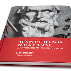 May include: A red hardcover book titled "Mastering Realism: Drawing Techniques for the Modern Tattoo Artist" by Lanny Markasky, featuring Mike DeVries. The cover features a black and white drawing of a man's face.