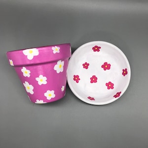 May include: Two terracotta flower pots, one pink with white flowers and one white with red flowers.