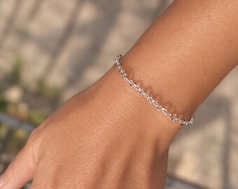 May include: A silver chain bracelet featuring a series of small, circular, textured links. The metal has a bright, reflective finish with a repeating pattern of fine, etched lines on each individual link, creating a delicate and uniform appearance.