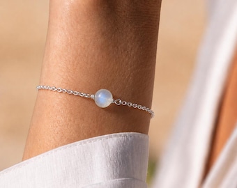 Puede incluir: Una delicada pulsera de cadena de plata que presenta una única cuenta de piedra lunar redonda y translúcida en el centro. Los eslabones de la cadena de metal pulido están conectados a la gema lisa e iridiscente, creando una joya sencilla y refinada.