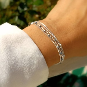 Peut inclure: Un bracelet argenté composé de plusieurs rangs de petites perles. Les perles sont un mélange d'argent et de bleu foncé.