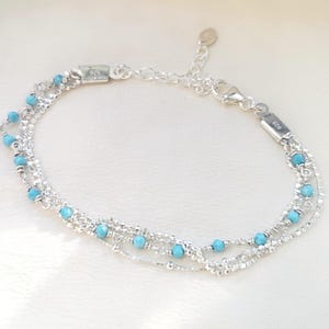 May include: A silver chain bracelet with turquoise beads. The bracelet has multiple strands and a lobster clasp closure.