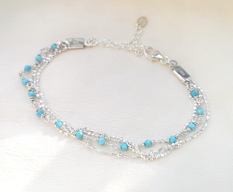 May include: A silver chain bracelet with turquoise beads. The bracelet has multiple strands and a lobster clasp closure.