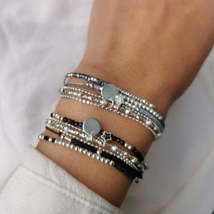 May include: A stack of silver bracelets with black beads and silver charms. The charms include a circle and a star.