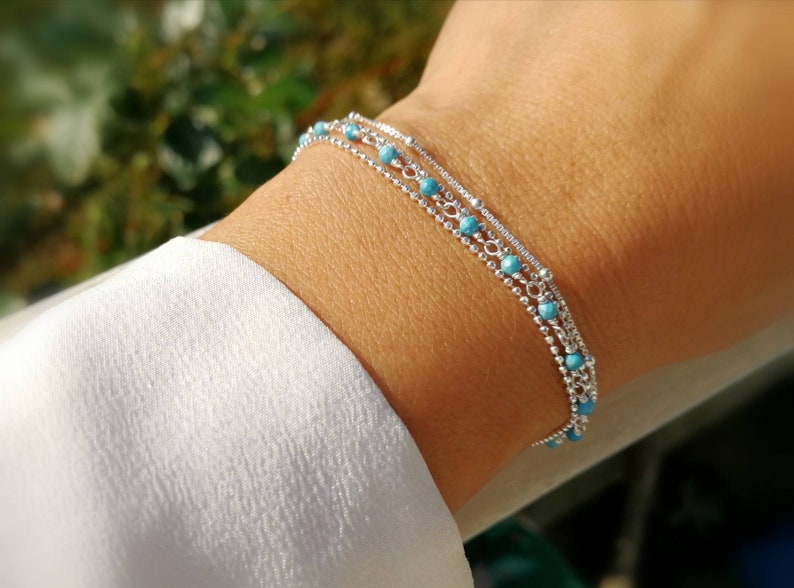May include: A silver bracelet with three strands of chain and turquoise beads.