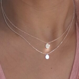 Op de afbeelding: Een zilveren ketting met twee delicate kettingen en twee kleine ronde hangers.