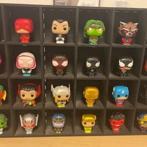 May include: A black display case with 20 small figurines of Marvel characters. The figurines are arranged in a grid pattern and include characters like Iron Man, Captain America, Spider-Man, and Thanos.