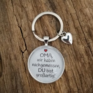 May include: A silver keyring with a round glass charm that says "OMA, wir haben nachgemessen, DU bist großartig!" with a red heart above the text. A small silver heart charm hangs from the keyring.