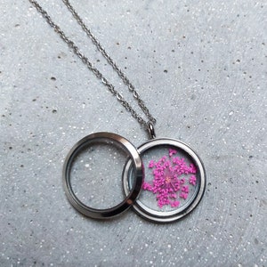 May include: A silver locket necklace with a clear glass locket that contains a pressed pink flower. The locket is open and the flower is visible.