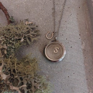 May include: Silver locket necklace with a small horseshoe charm. The locket is open and contains a lock of hair with the letter "S" engraved inside.