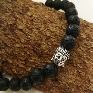 Könnte beinhalten: Schwarzes Lava-Stein-Armband mit einem silbernen Buddha-Kopf-Anhänger.