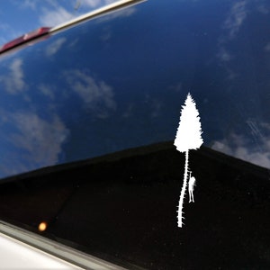 May include: A white vinyl sticker of a silhouette of a person climbing a tree. The sticker is on a car window with a blue sky reflected in the glass.