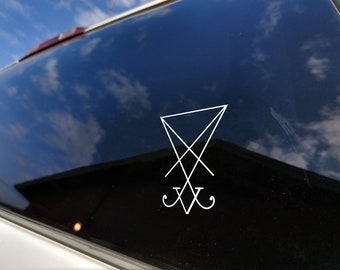 May include: White vinyl decal of the Sigil of Lucifer, a symbol associated with Luciferianism. The decal is applied to a dark, reflective surface, likely a car window. The sky and clouds are reflected in the window.