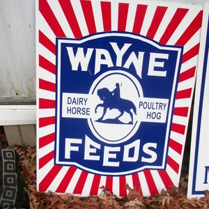 May include: A red, white, and blue sign with the text "WAYNE FEEDS" in a blue circle. The sign also has the text "DAIRY HORSE" and "POULTRY HOG" in smaller text.