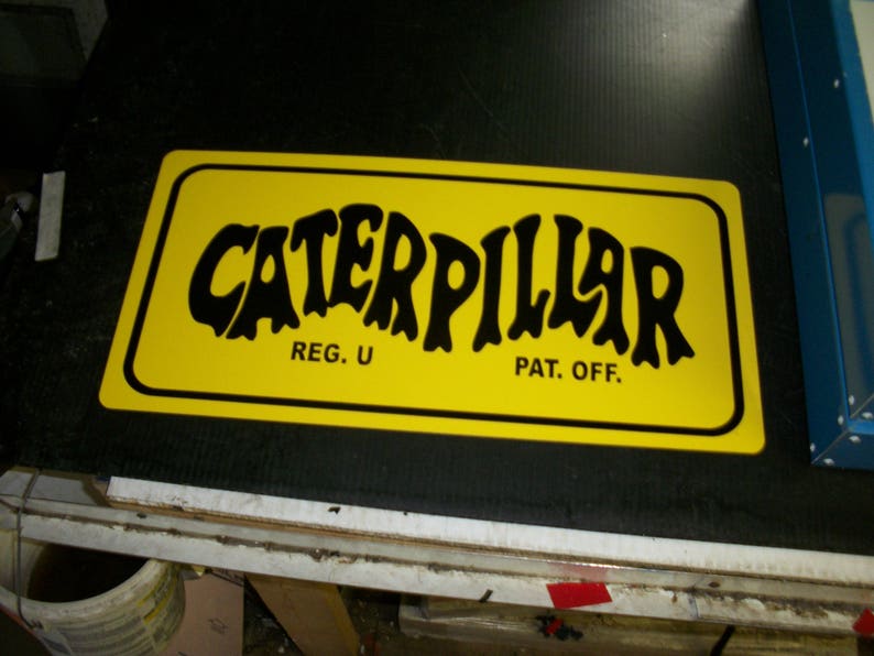 May include: A yellow sign with black text that reads "Caterpillar" with "Reg. U" and "Pat. Off." underneath.