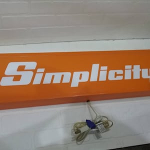 May include: Orange sign with the word "Simplicity" in white lettering.