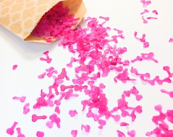 Könnte beinhalten: Eine beigefarbene Papiertüte mit weißem Vierpassmuster, aus der zahlreiche kleine, leuchtend pinke, phallisch geformte Konfettistücke herausfallen. Das Konfetti ist auf der Oberfläche verstreut und erzeugt ein lebhaftes Bild neonpinker Formen.