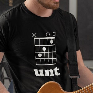 Könnte beinhalten: Ein schwarzes T-Shirt mit einem weißen Gitarrenakkorddiagramm und dem Wort "unt" darauf gedruckt. Die Person, die das Shirt trägt, spielt Gitarre.