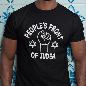 May include: A black t-shirt with a white graphic design that says "People's Front of Judea" with a raised fist and two Star of David symbols.