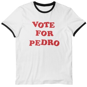 Op de afbeelding: Wit T-shirt met een zwarte boord en rode tekst die "VOTE FOR PEDRO" zegt.