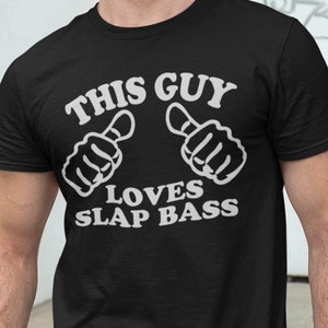 Peut inclure: Un t-shirt noir avec du texte blanc qui dit "This Guy Loves Slap Bass". Le texte est entouré de deux pouces en l'air blancs.