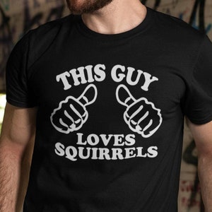 Może przedstawiać: Czarny T-shirt z białym napisem "This Guy Loves Squirrels". Tekst jest otoczony dwoma białymi ikonami kciuków w górę.