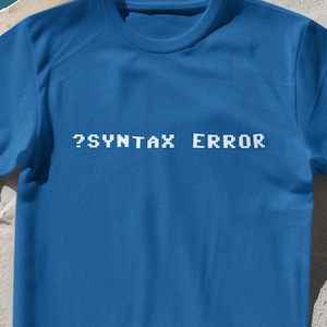 May include: A royal blue t-shirt with the text "?SYNTAX ERROR" printed in white on the front.