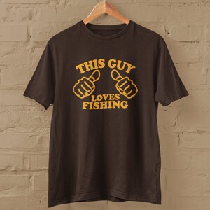 May include: A brown t-shirt with the text "This Guy Loves Fishing" in yellow lettering. Two yellow thumbs up are above the text.