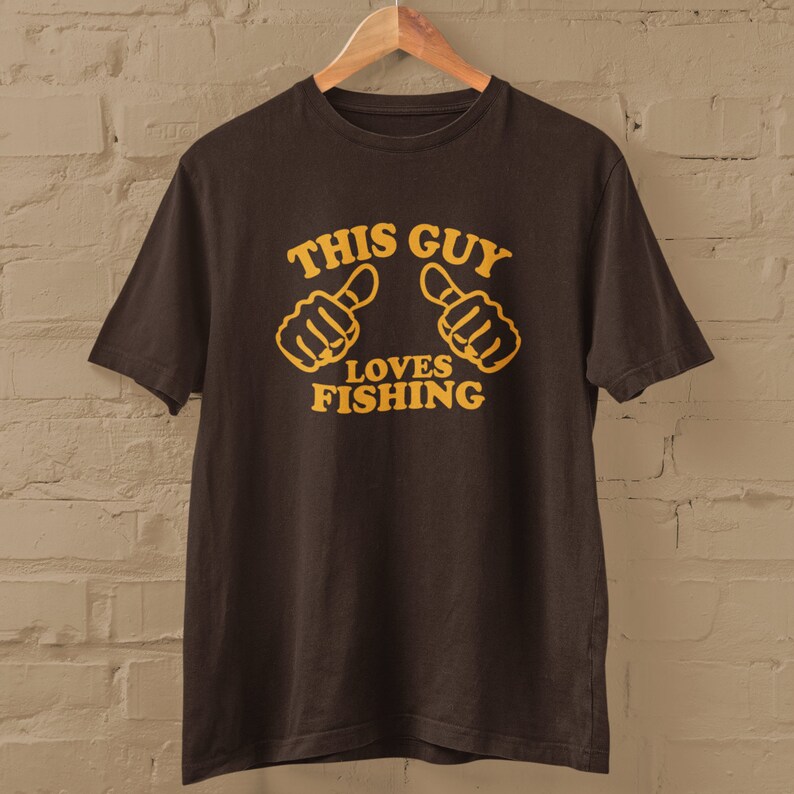 May include: A brown t-shirt with the text "This Guy Loves Fishing" in yellow lettering. Two yellow thumbs up are above the text.