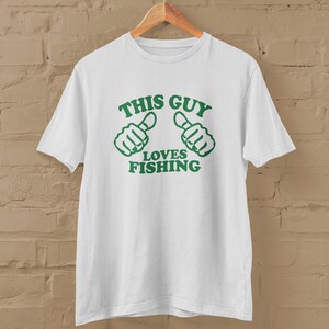 May include: White t-shirt with green text that reads "This Guy Loves Fishing" and two green thumbs up icons.