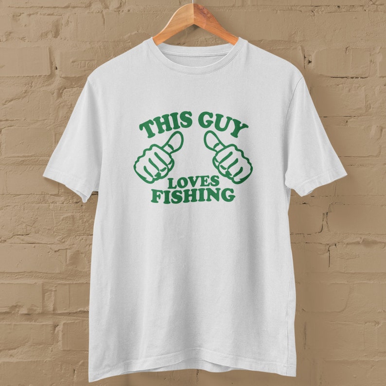 May include: White t-shirt with green text that reads "This Guy Loves Fishing" and two green thumbs up icons.