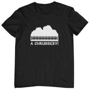 May include: Black t-shirt featuring a white graphic of a shrubbery and a picket fence. The text "A SHRUBBERY!" is printed in white below the graphic. The shirt is made of a soft material.