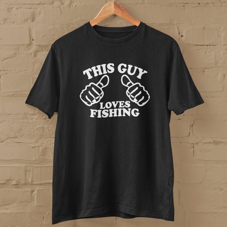 May include: Black t-shirt with white text that reads "This Guy Loves Fishing" and two thumbs up.