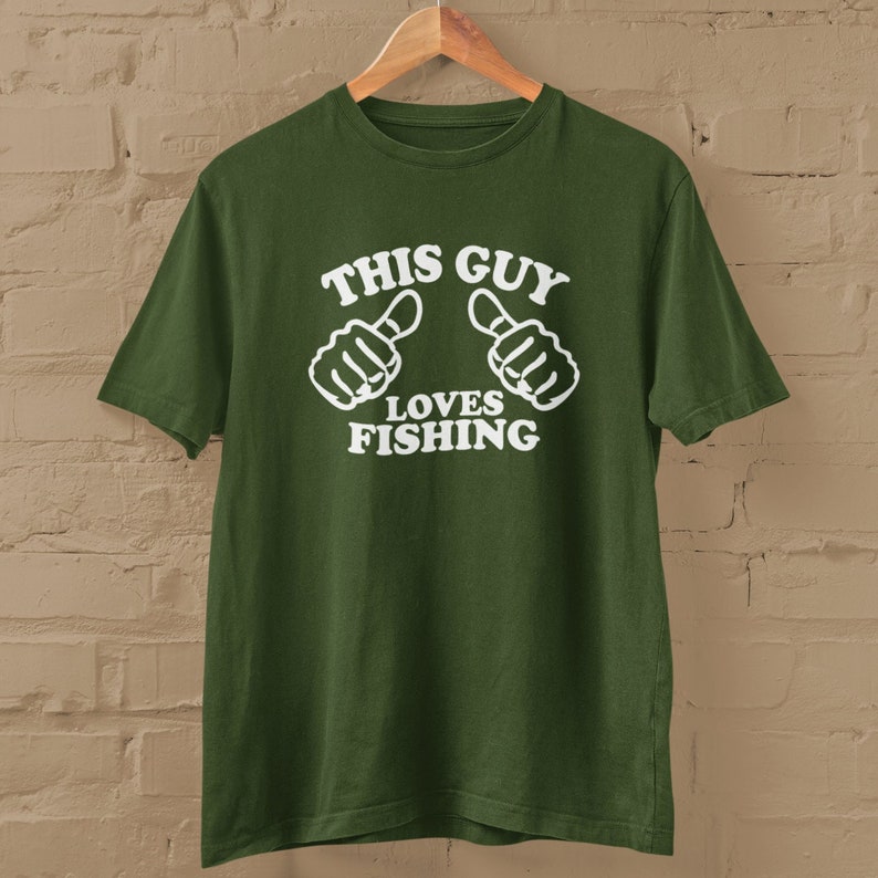 May include: A green t-shirt with white text that reads "This Guy Loves Fishing" and two white thumbs up.