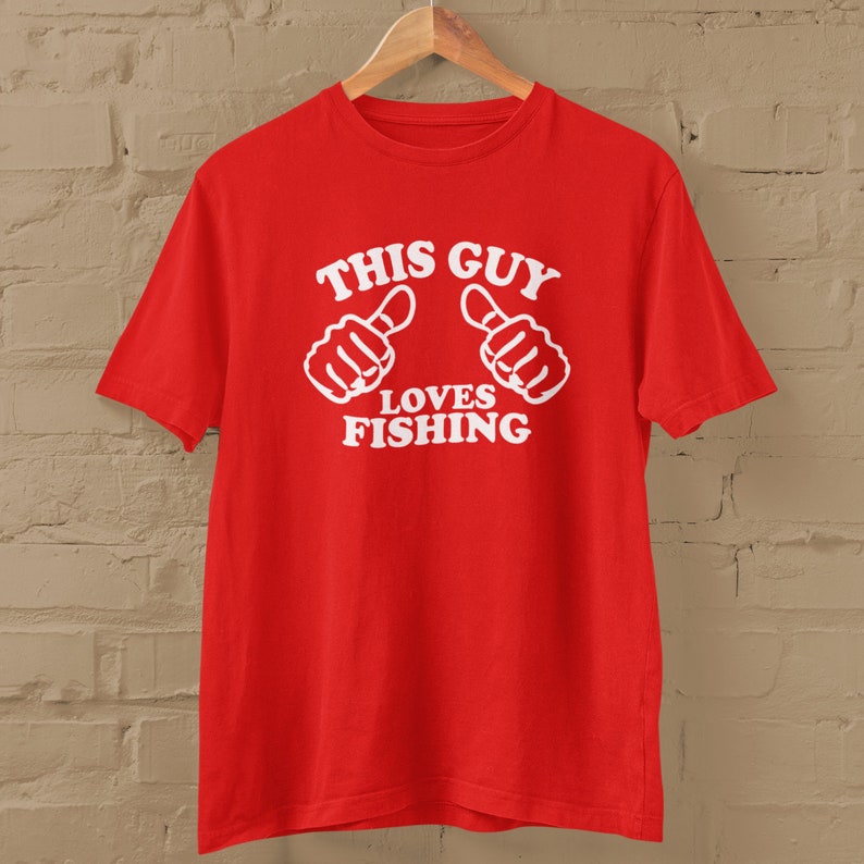 May include: Red t-shirt with white text that says "This Guy Loves Fishing" and two white thumbs up.