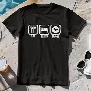 Könnte beinhalten: Schwarzes T-Shirt mit einem weißen Grafikdesign. Die Grafik zeigt drei Symbole mit den Wörtern "Essen", "Schlafen" und "Feiern" darunter.