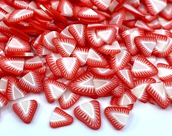 May include: A large pile of red and white strawberry slice shaped polymer clay charms. The charms are perfect for adding a touch of sweetness to your crafts.