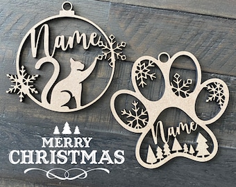 May include: Two wooden Christmas decorations, one shaped like a paw print and the other like a circle with a cat inside. Both decorations have the word "Name" written on them and are decorated with snowflakes. The paw print decoration also has small trees at the bottom. The text "Merry Christmas" is written below the decorations.