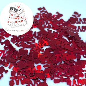May include: Red glitter confetti shaped like the word "love" on a white background.